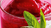 A close-up of a glass filled with red sorbet with mint leaves as garnish and a small bowl of white sorbet beside it.