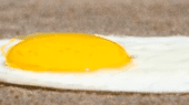 A fried egg with a runny yolk and cooked whites is lying on a sandy surface.