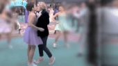 Two people kiss on a colorful dance floor, surrounded by blurred figures in bright clothing in the background.