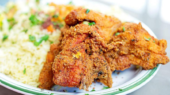 A plate with fried chicken pieces and a side of seasoned rice garnished with chopped herbs.