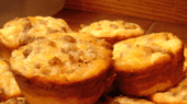 A plate of golden-brown muffins topped with melted cheese and bits of ground meat, positioned on a tiled countertop.