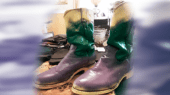 A pair of two-tone boots with purple and green leather standing on a patterned surface. The background is blurred.