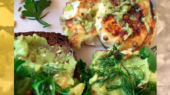 A plate with an omelet and slices of toast topped with mashed avocado, garnished with parsley and dill.