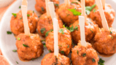 A plate of meatballs with wooden picks garnished with chopped herbs.