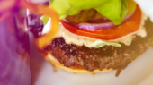 Close-up of a hamburger with a beef patty, lettuce, tomato, pickles, red onion, and sauce on a plate.