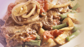 Close-up of a beef dish with sliced onions, tomatoes, green beans, and mushrooms in a savory sauce.