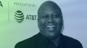 A man in a suit smiles at an event with a Tribeca Film Festival and AT&T logo in the background.