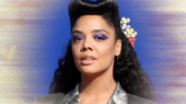 Person with styled hair and purple eye makeup wearing a silver jacket stands against a gradient background.