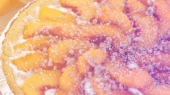 Close-up of a peach pie with a crumbly topping, showcasing fresh peach slices arranged on top of a creamy filling within a pie crust.