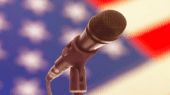 A microphone is positioned in front of a blurred American flag backdrop.