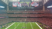 A football game at NRG Stadium, with the scoreboard displaying "4th Quarter." The field is lined with players, and the stands are packed with spectators.