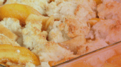 Close-up view of a peach cobbler in a baking dish, showing golden brown biscuit topping and baked peach slices.