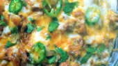 Close-up of a cheesy casserole topped with green jalapeño slices and fresh cilantro.