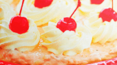 A close-up of a dessert with whipped cream topped with cherries on a creamy base, served in a red dish.