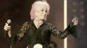 A woman with pink hair and black shirt on stage.