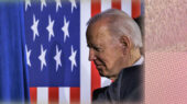 Joe Biden walking on a stage with a huge American flag