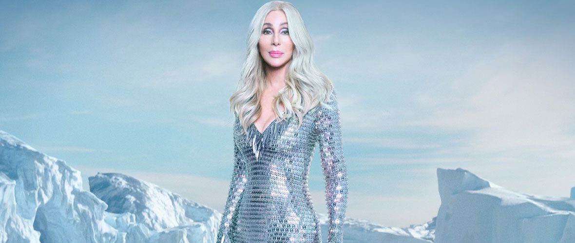 A woman in silver dress standing next to snow covered mountains.