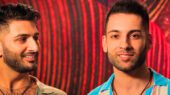 Two men posing for a picture in front of a red background.